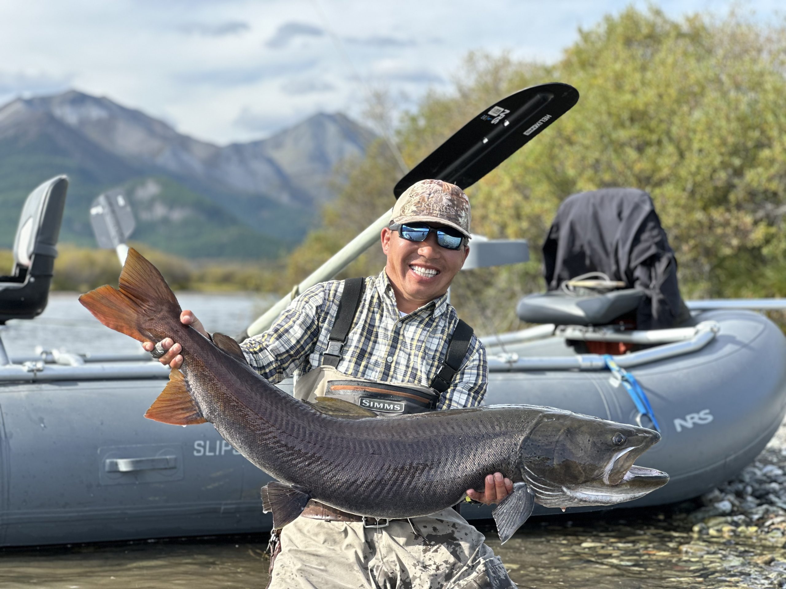 Angler holding a taimen beside a raft